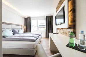 Una habitación de hotel moderna con cama, escritorio, televisor de pantalla plana y ventana con cortinas.