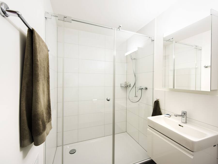 A modern bathroom with a glass shower enclosure, a white sink, and a towel hanging on a rack.