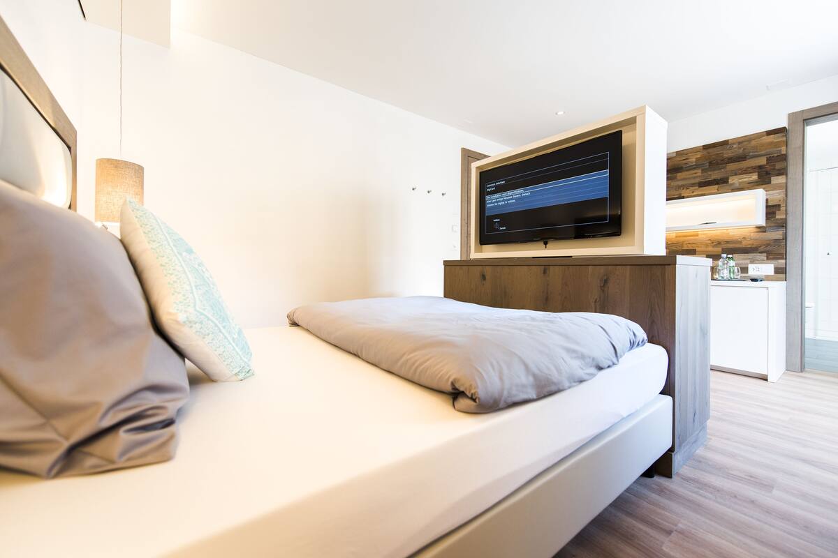A modern hotel room with a bed, a flat-screen TV mounted above it, and a wooden accent wall.