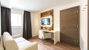 Una habitación moderna con un sofá blanco, un escritorio con una computadora, un televisor montado en una pared de madera y una puerta grande de madera.