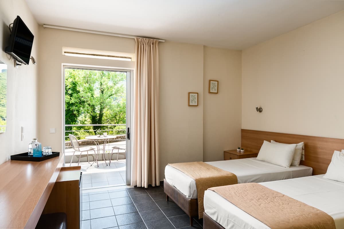 Une chambre d’hôtel avec deux lits, un bureau, une télévision et un balcon donnant sur la forêt.