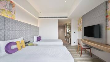 A hotel room with two beds, a TV, a desk, and a bathroom visible through an open door.