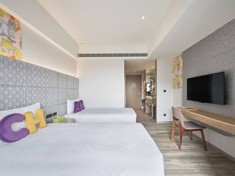 A hotel room with two beds, a TV, a desk, and a bathroom visible through an open door.