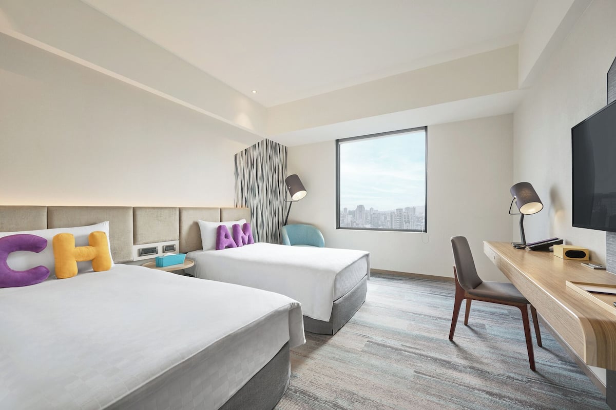 Une chambre d’hôtel avec deux lits, un bureau, une chaise et une grande fenêtre.