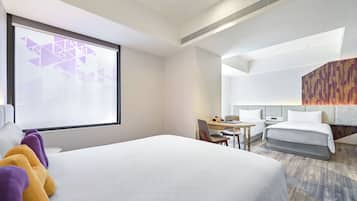 A hotel room with a large bed, a desk, a chair, and a window with a geometric view.