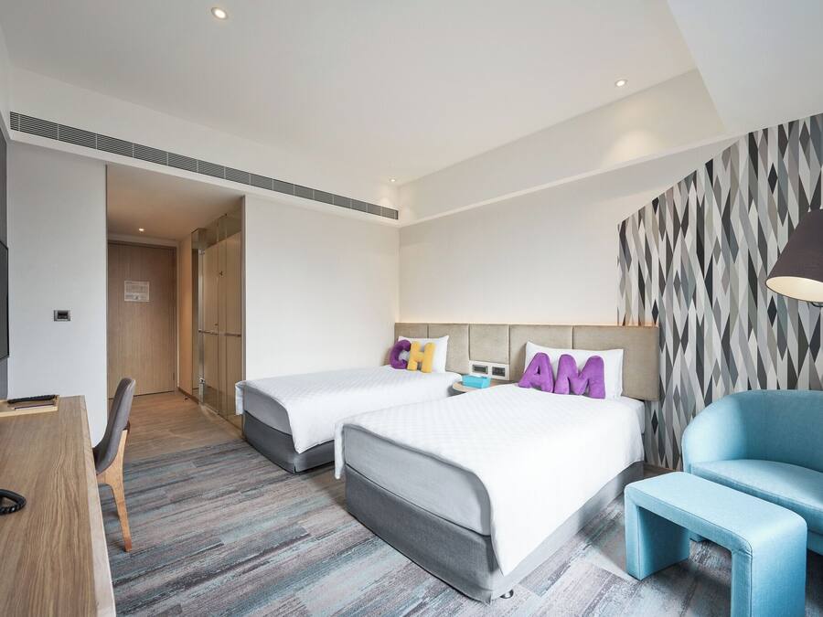 Une chambre d’hôtel avec deux lits, un bureau, une chaise, une lampe et un mur décoré de motifs.