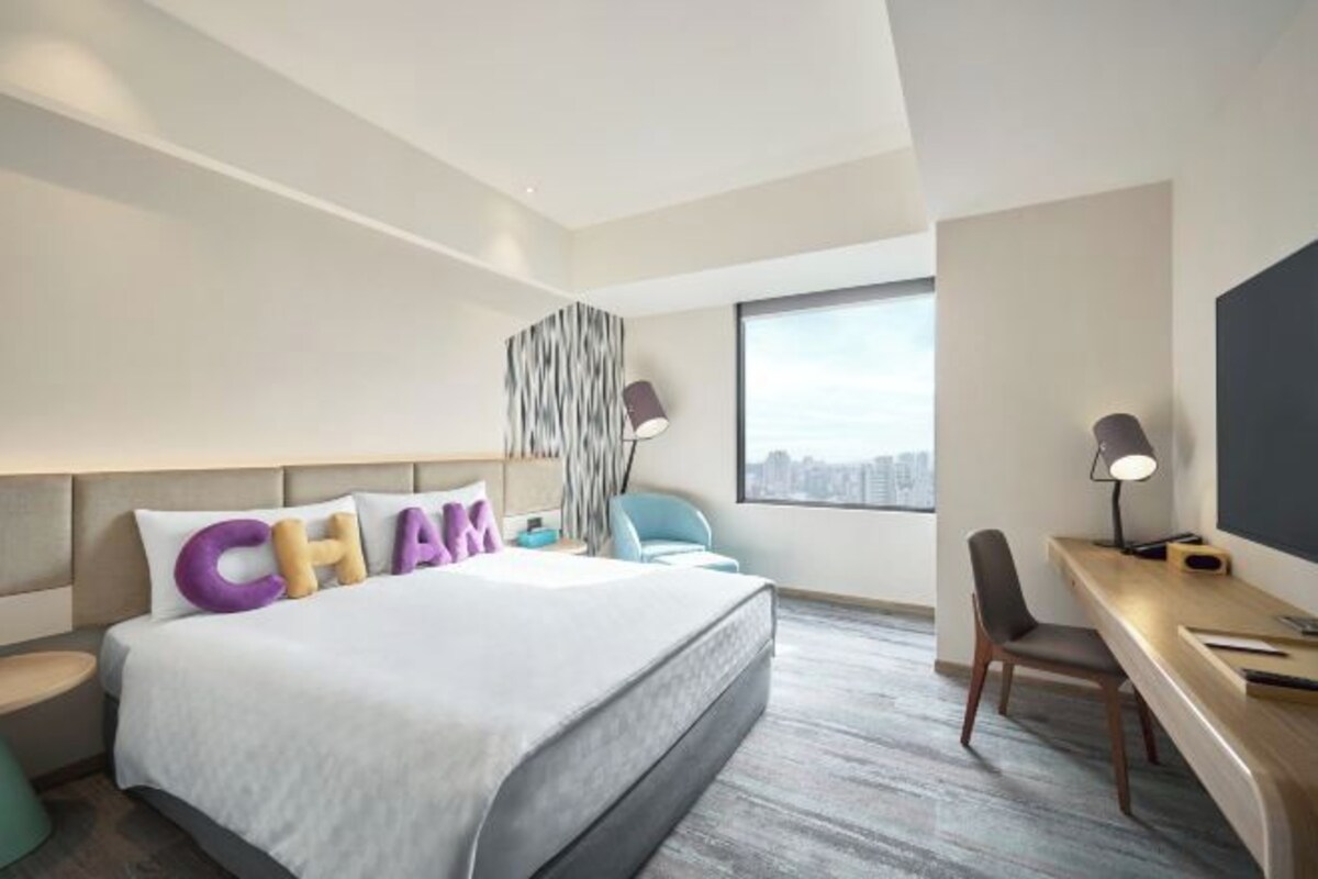 A modern hotel room with a large bed, a desk, a chair, and a city view.