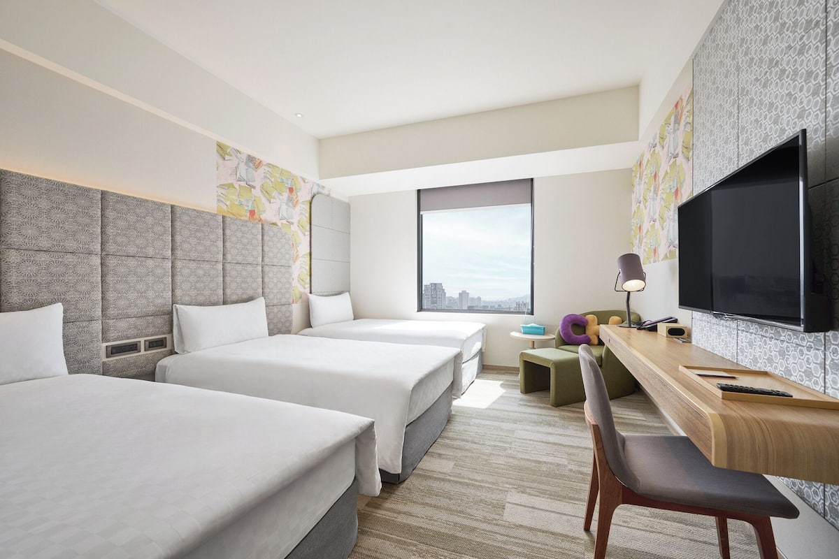Une chambre d’hôtel avec deux lits, un bureau avec une chaise, une télévision et une fenêtre donnant sur la ville.