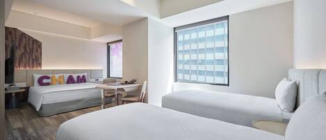 A hotel room with two beds, a desk, a chair, a TV, and a large window.