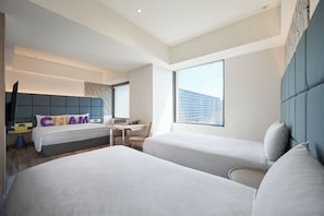 Ein Hotelzimmer mit zwei Betten, einem Schreibtisch, einem Stuhl, einem großen Fenster und Blick auf die Stadt.