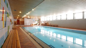 An indoor swimming pool with tiled walls, wooden benches, and a tiled floor. - Sport Hotel Pampeago (Tesero)