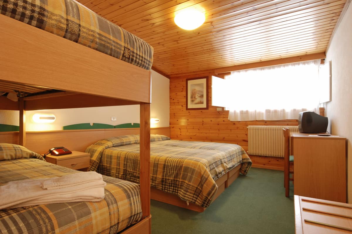 A room with bunk beds, a desk, a chair, a radiator, and a window with curtains.