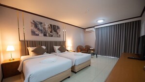 Quarto de hotel com duas camas, uma escrivaninha, televisão e uma janela grande com cortinas.