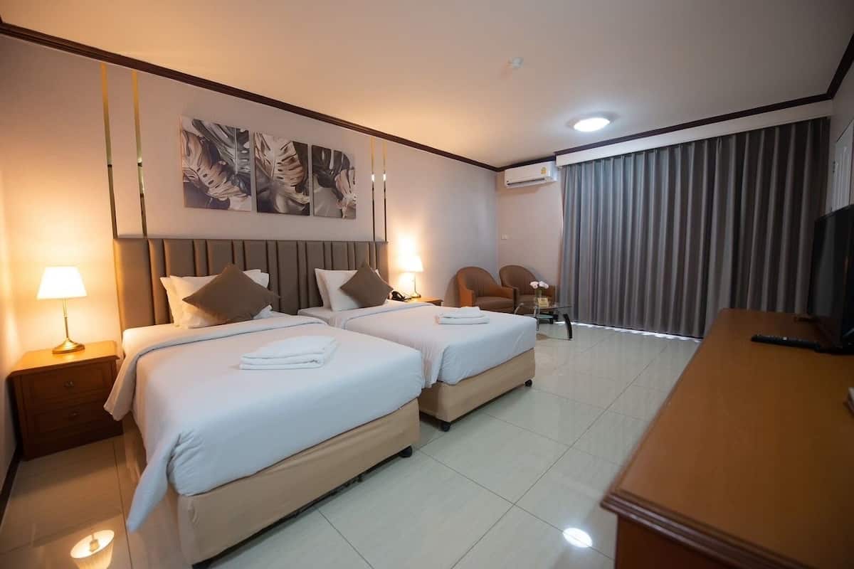 A hotel room with two beds, a desk, a TV, and a large window with curtains.