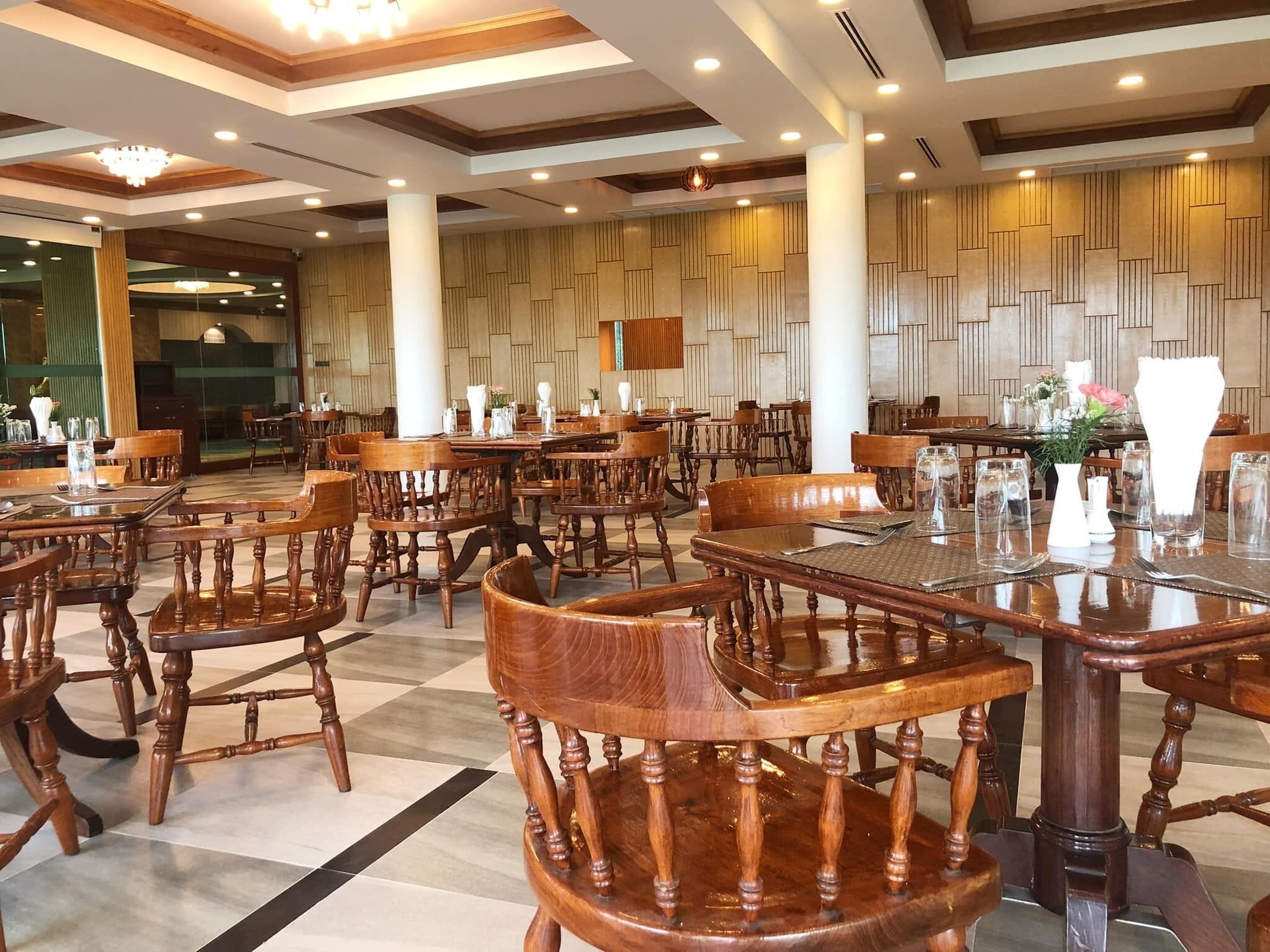 A spacious dining area with wooden tables and chairs, a patterned wall, and a chandelier.