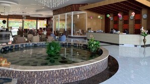 Um saguão de hotel com balcão de recepção, área de estar e um elemento central de água.