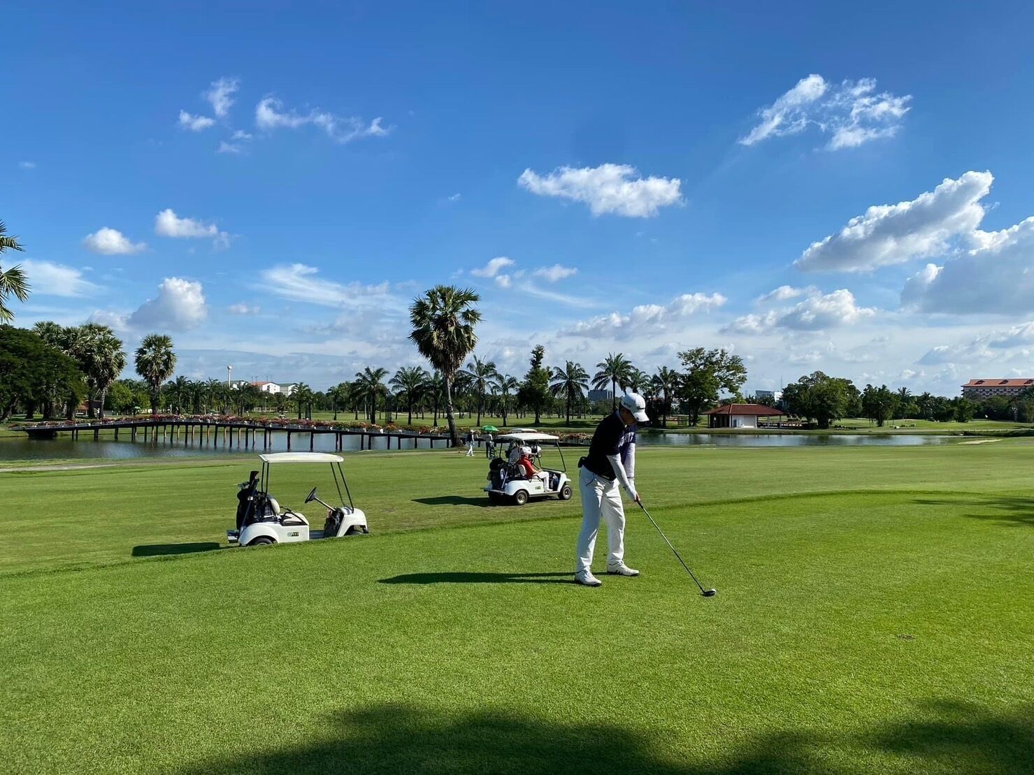 Un campo de golf con cielo despejado, palmeras y una masa de agua al fondo.