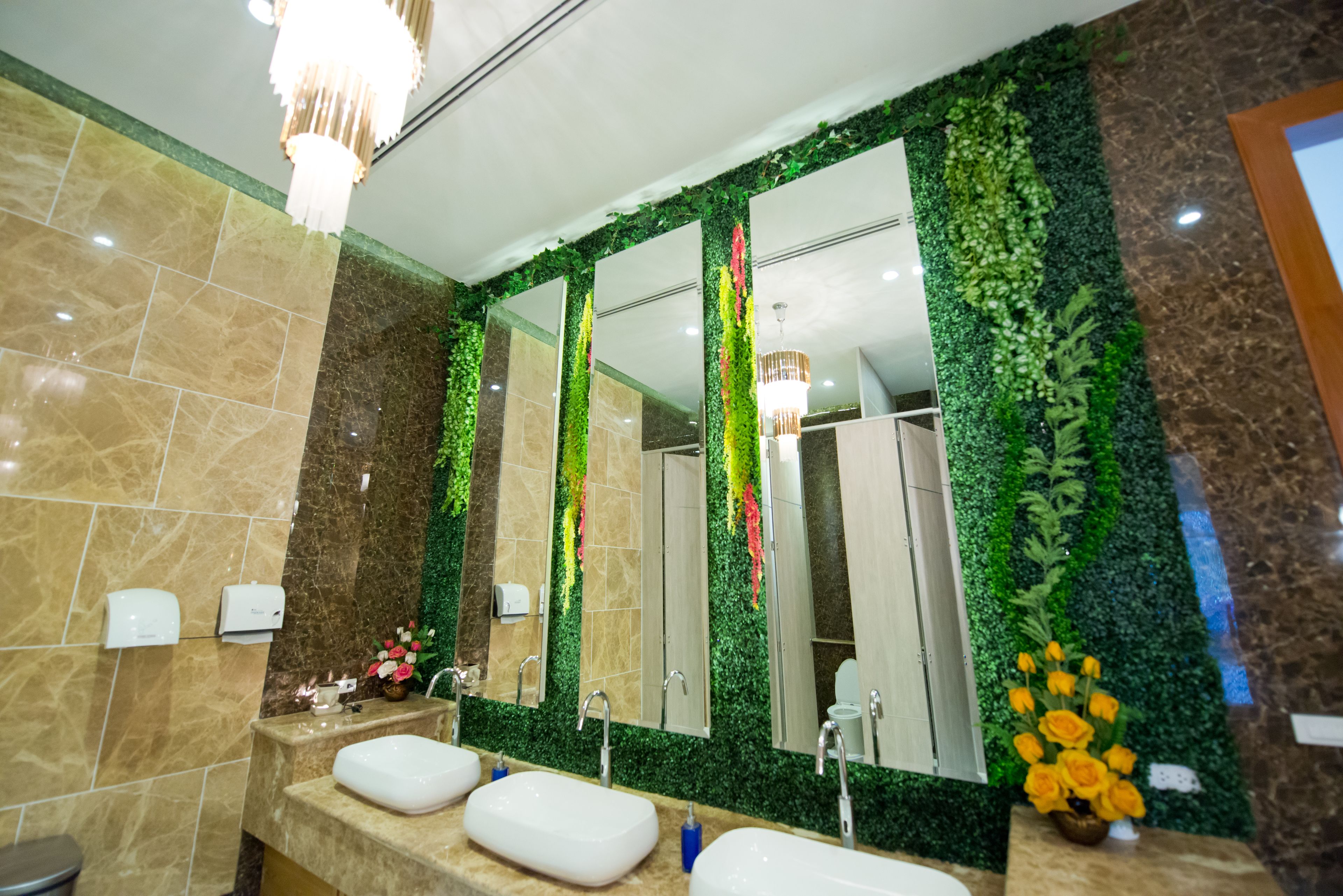 A bathroom with three sinks, a large mirror, and green foliage on the walls.