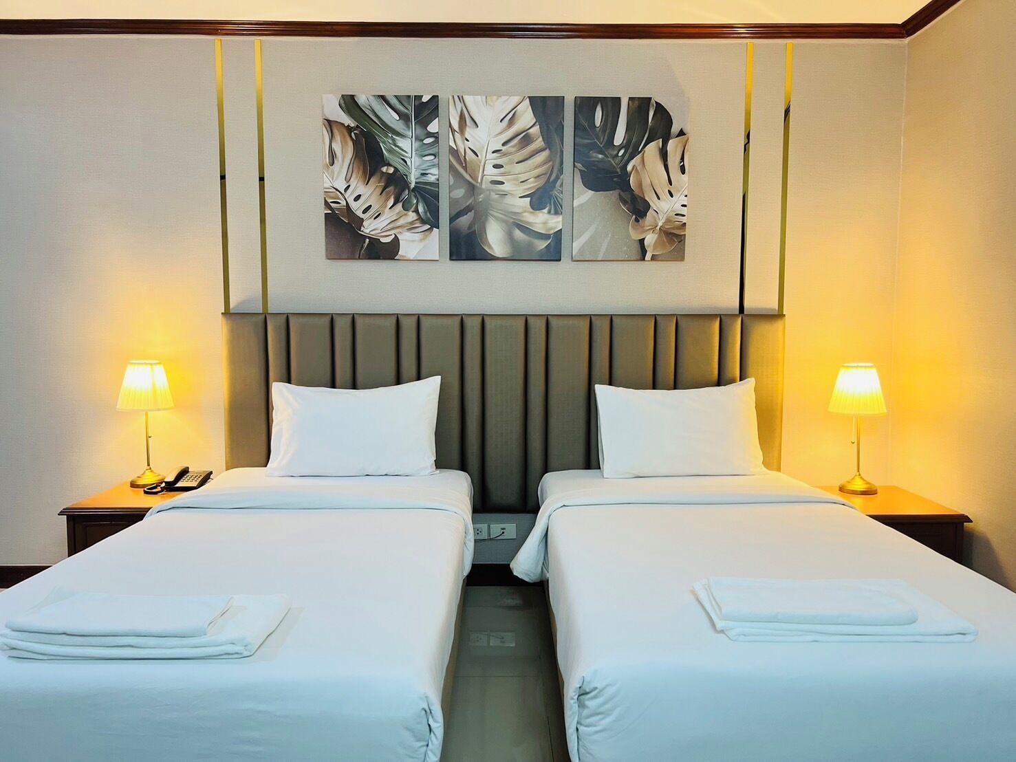 Ein Hotelzimmer mit zwei Einzelbetten, einem Kopfteil, Nachttischlampen, einem Telefon und einem Wandbild.