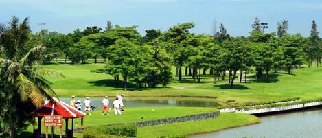 Un campo de golf con un estanque, árboles y un pabellón.