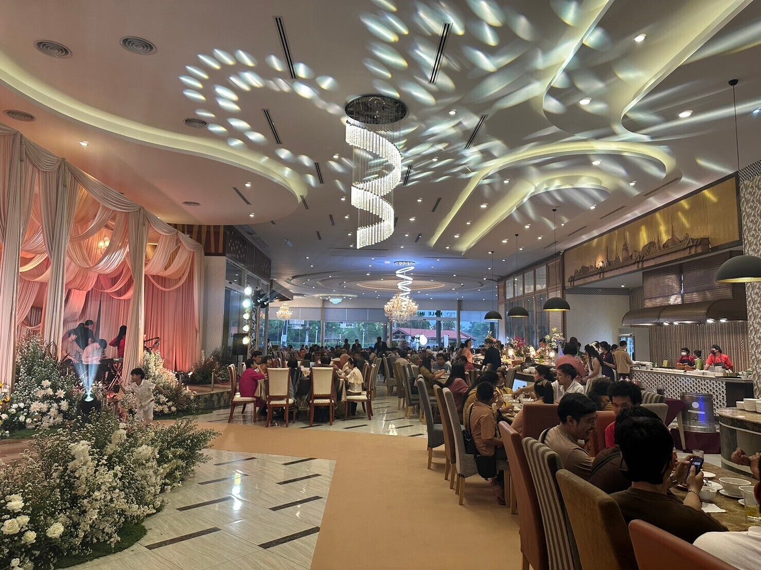 A spacious restaurant with a modern ceiling design, a stage for performances, and a well-lit dining area.
