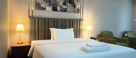 Habitación de hotel con una cama grande, dos lámparas de noche, una silla y un teléfono instalado en la pared.