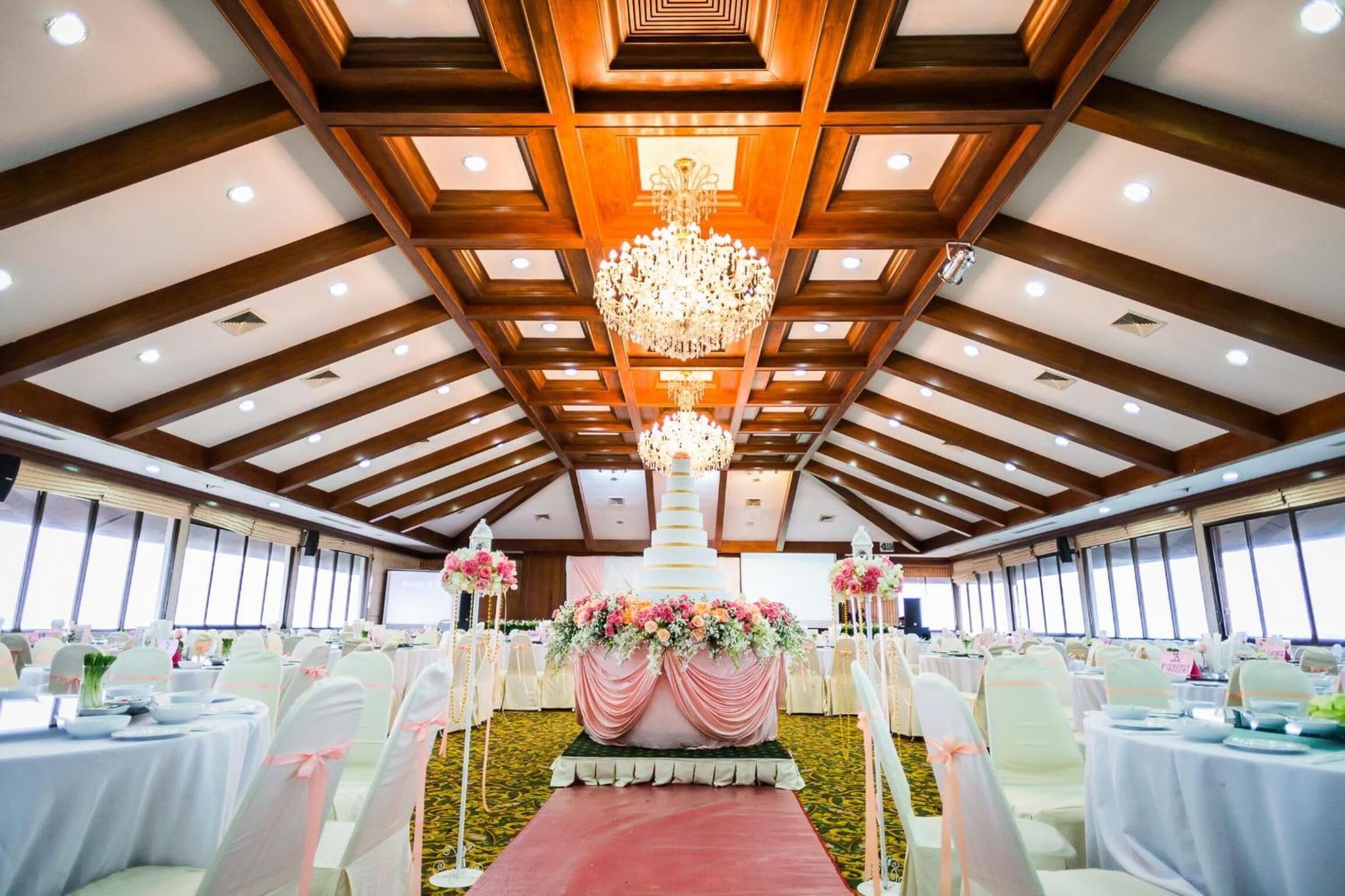 A banquet hall with round tables, white chairs, and a large floral centerpiece.