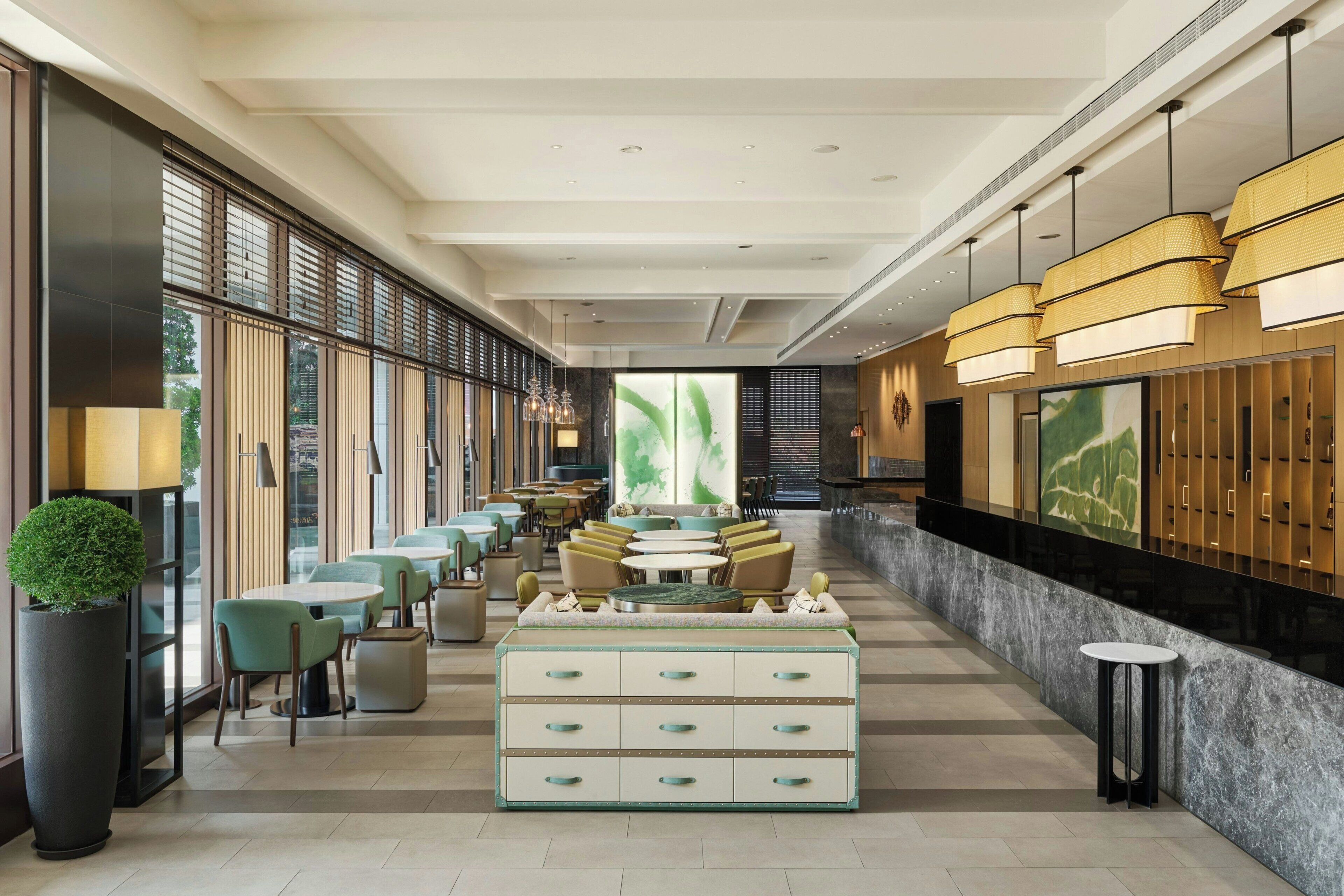 A modern hotel lobby with a long reception desk, seating area, and large windows.