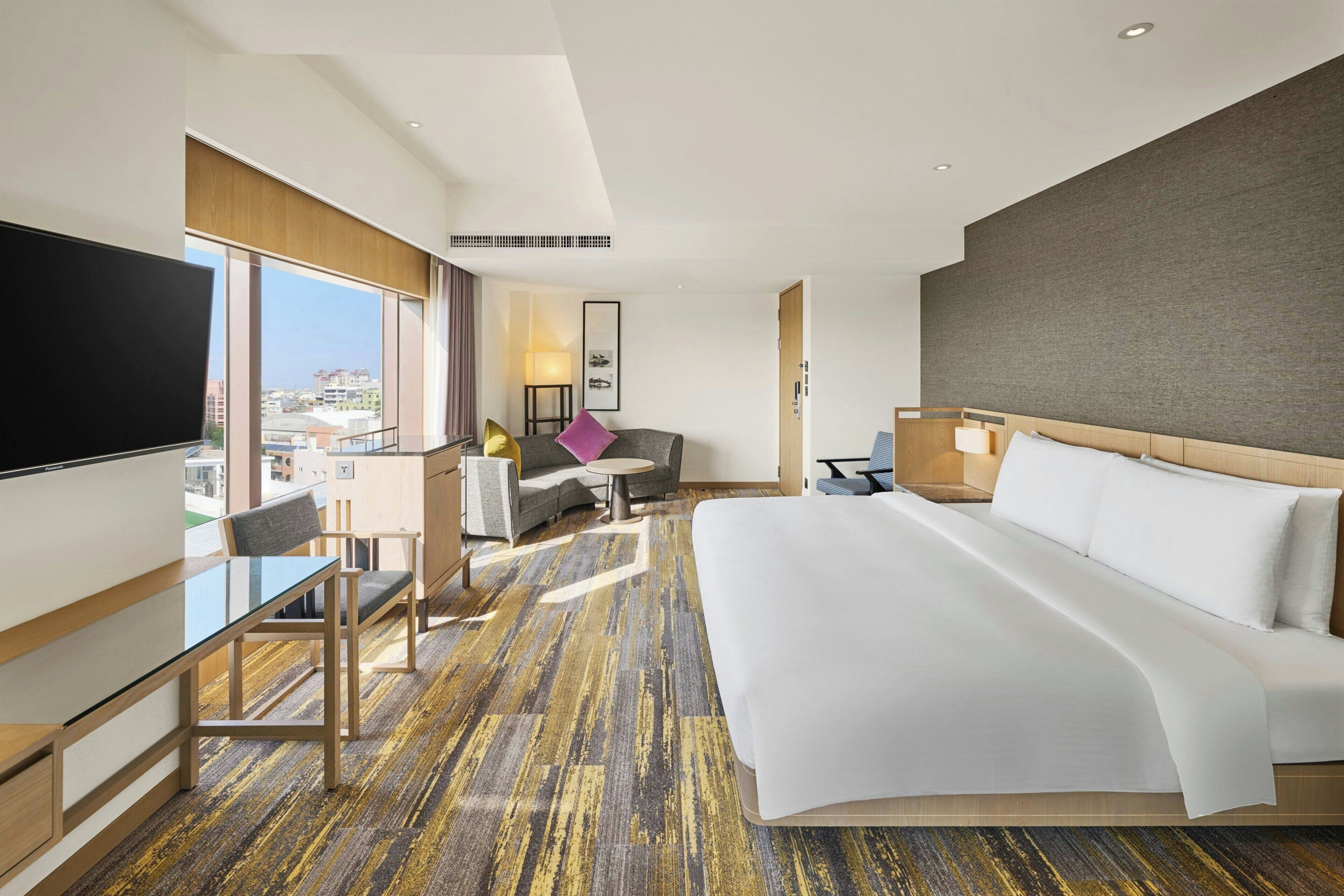 Une chambre d’hôtel moderne dotée d’un grand lit, d’un bureau, d’une chaise, d’une télévision et offrant une vue sur la ville.