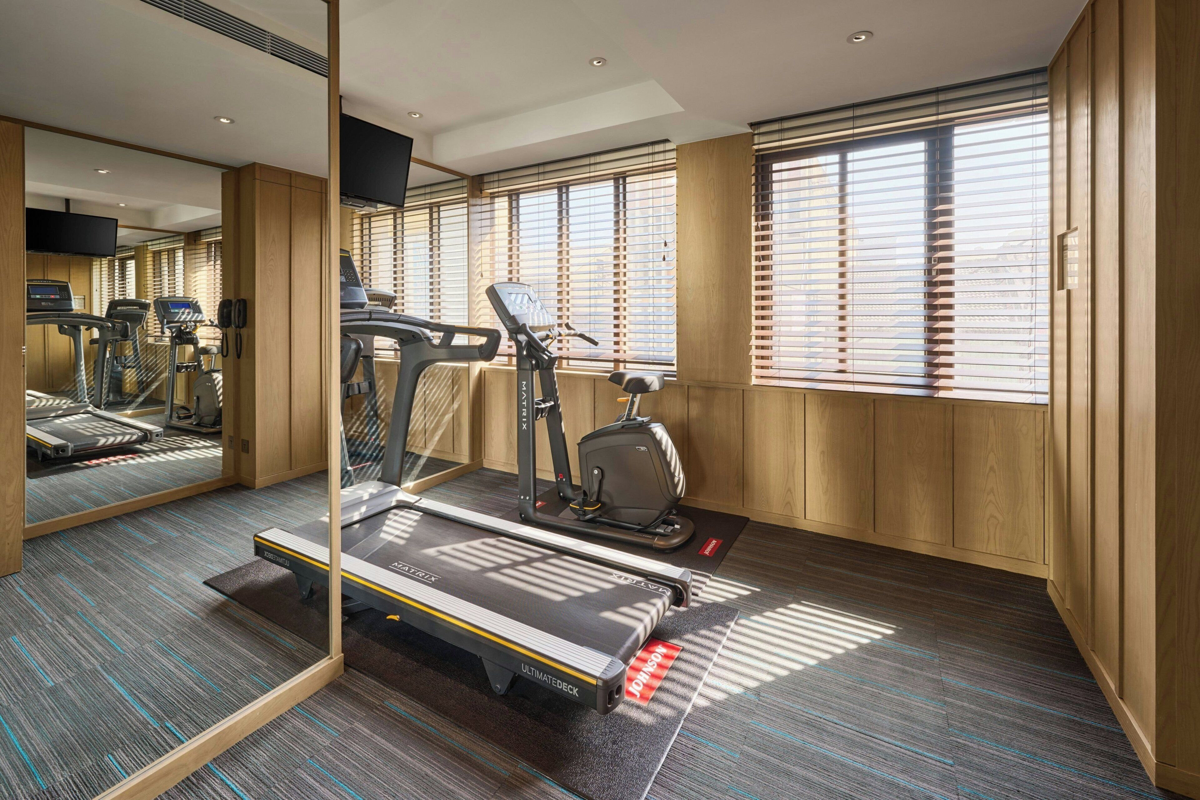A hotel room with a treadmill, exercise bike, and a mirror reflecting the room.