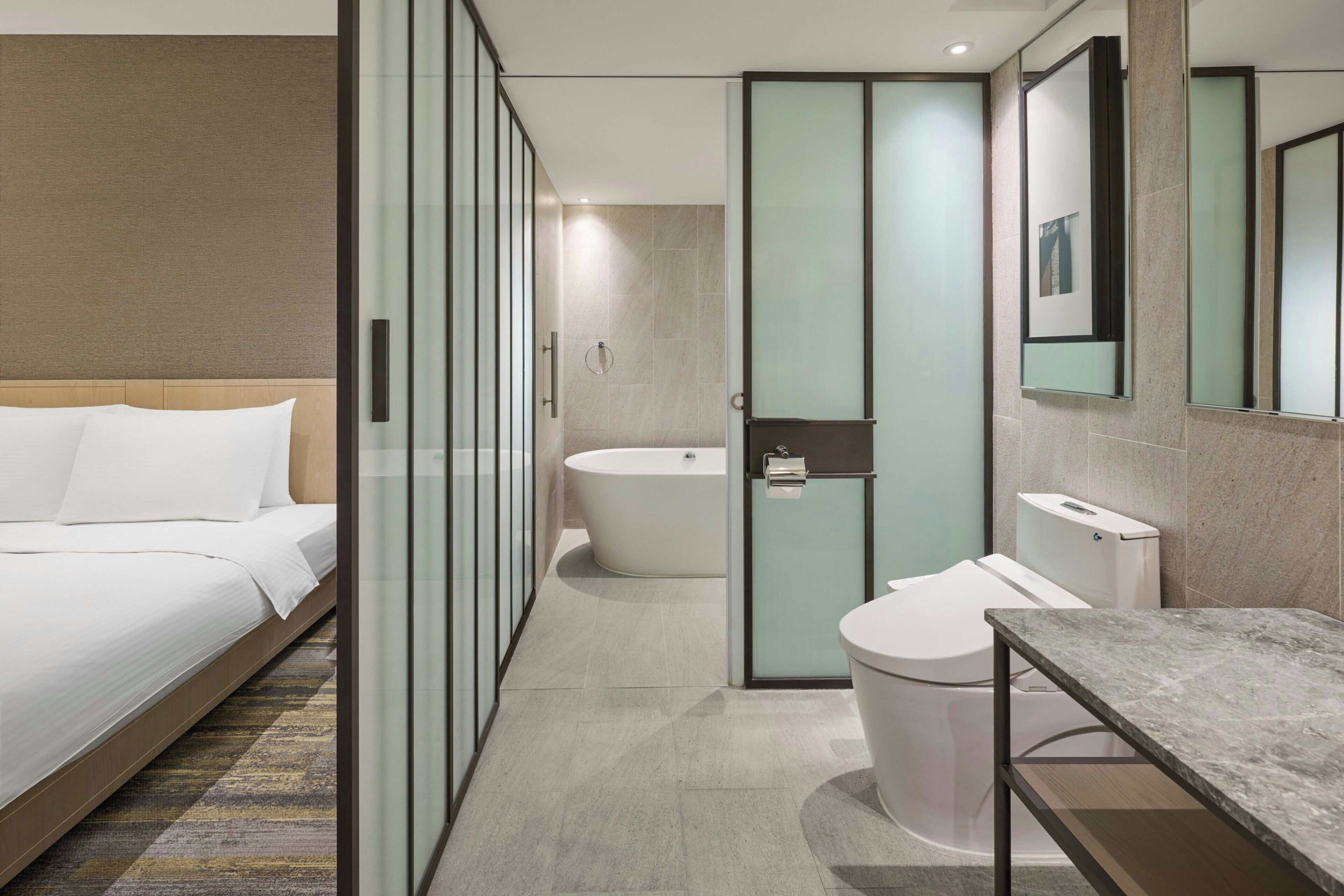 Una camera d'albergo moderna con un letto, un bagno con vasca, water e lavandino.
