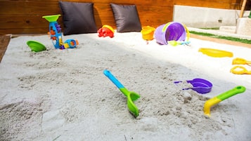 A sandy play area with various toys and a wooden wall in the background.