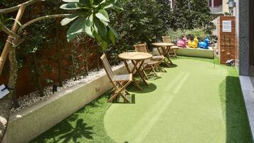 A patio with artificial grass, wooden chairs, and tables.