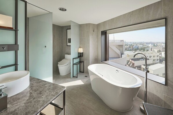 A modern bathroom with a freestanding bathtub, a large mirror, and a view of the cityscape.