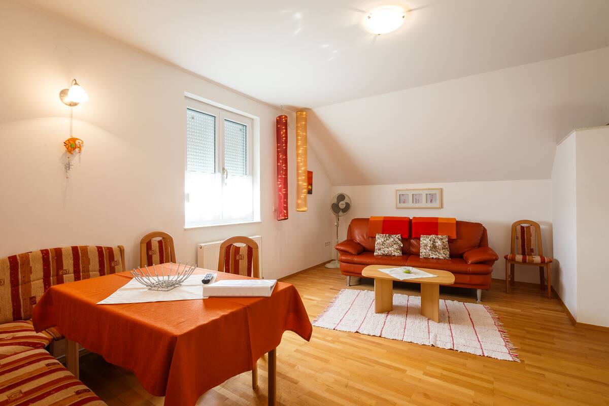 A living room with a dining table, a sofa, a coffee table, and a window with blinds.