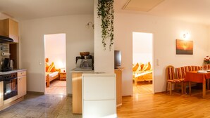 A modern kitchen with wooden cabinets, a built-in oven, and a refrigerator. There is a dining area with a wooden table and chairs, and a cozy seating area with a sofa and a TV. - Appartmenthaus Freiler (Morbisch am See)
