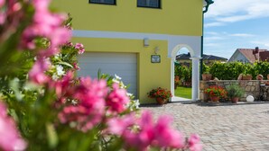 A yellow building with a garage door, potted plants, and a stone wall. - Appartmenthaus Freiler (Morbisch am See)