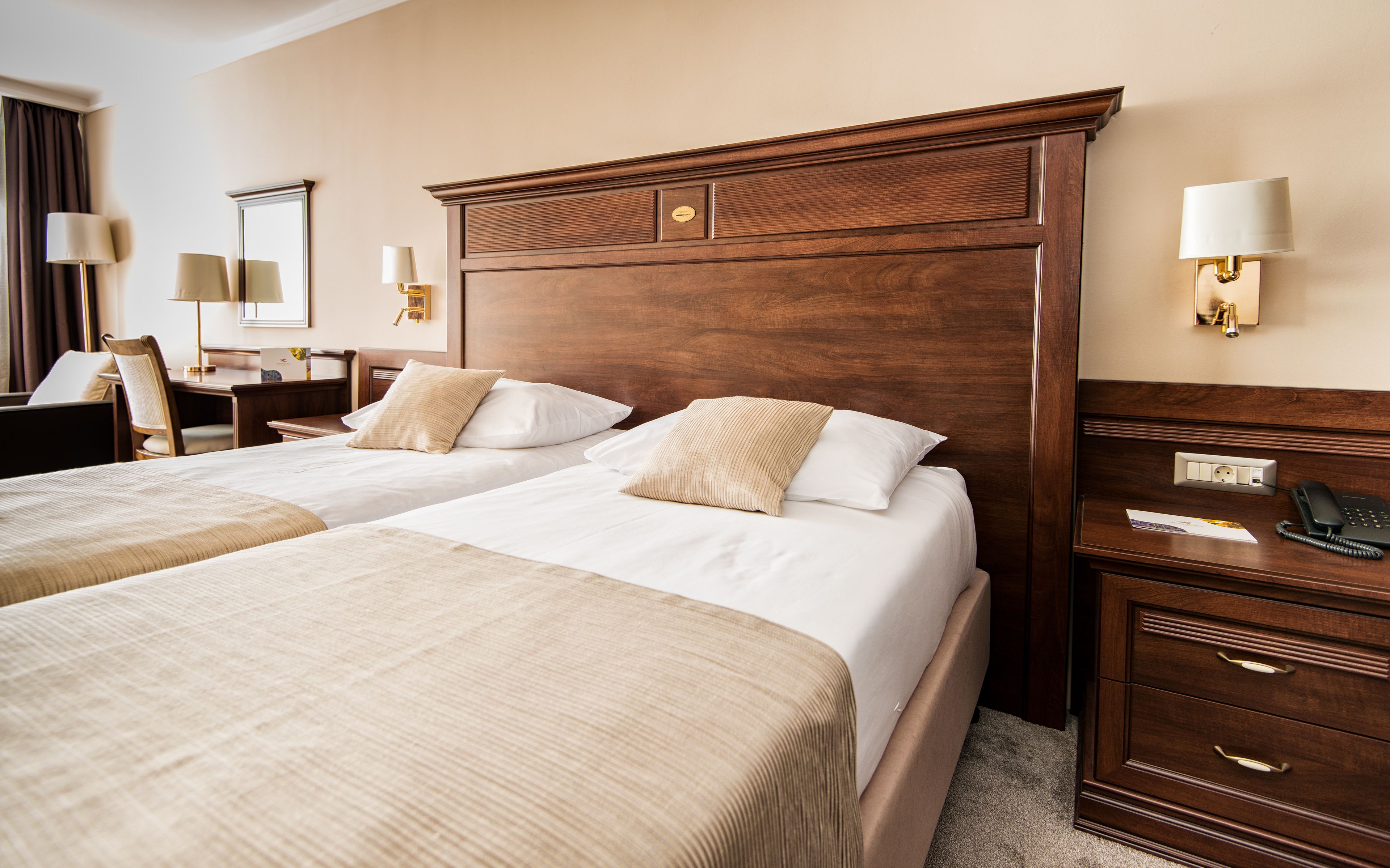 Een hotelkamer met twee bedden, een houten hoofdeinde, nachtlampjes, een bureau en een telefoon.