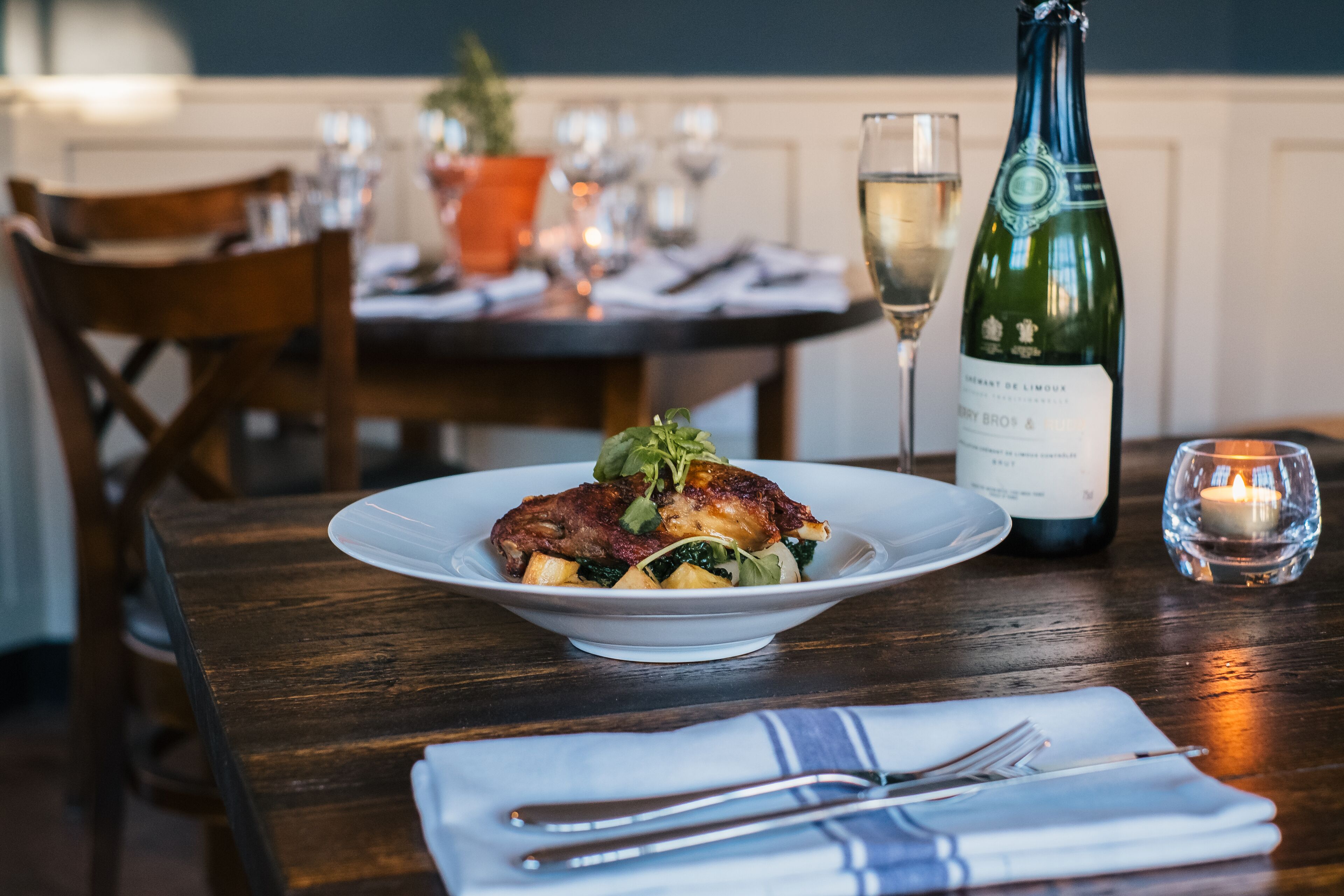 Une table à manger avec une assiette de nourriture, une bouteille de vin et une bougie.