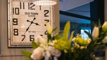 A bar area with a vintage clock, a vase with flowers, and a bowl of oranges.