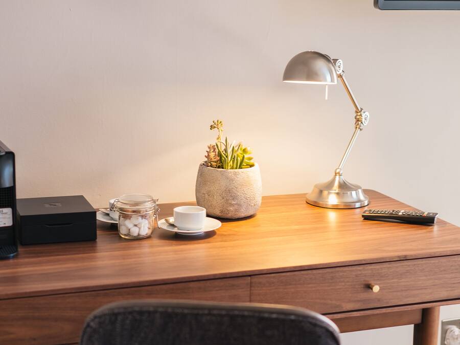 A wooden desk with a lamp, a potted plant, a cup, and a remote control.