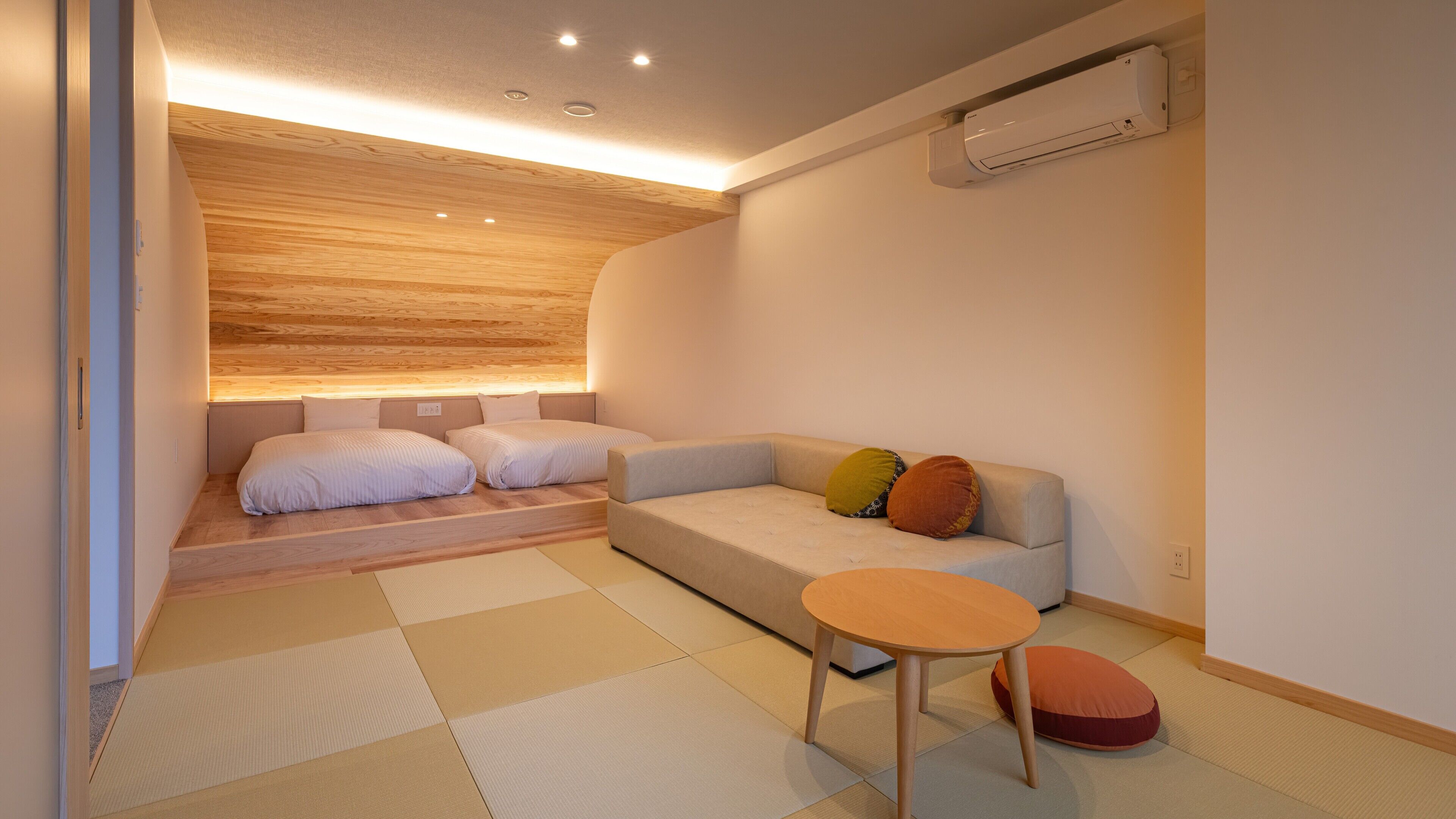 A modern room with a sofa, a small table, tatami mats, and an air conditioning unit.