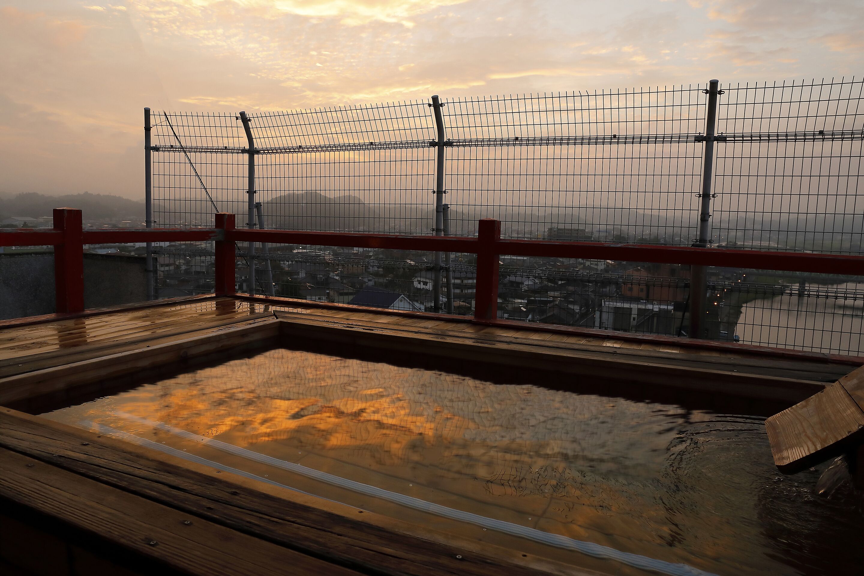 A wooden deck with a metal fence and a view of a cityscape in the background.