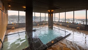 A large indoor pool with a view of a cityscape through large windows. - Shokyoto No Yu Mikuma Hotel (Hita)