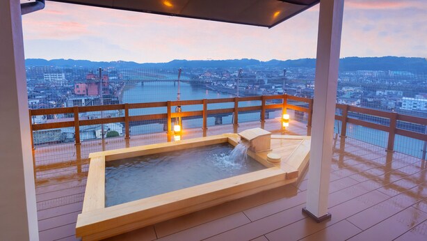 A hot tub on a wooden deck with a city view, a railing, and a sunset in the background. - Shokyoto No Yu Mikuma Hotel (Hita)