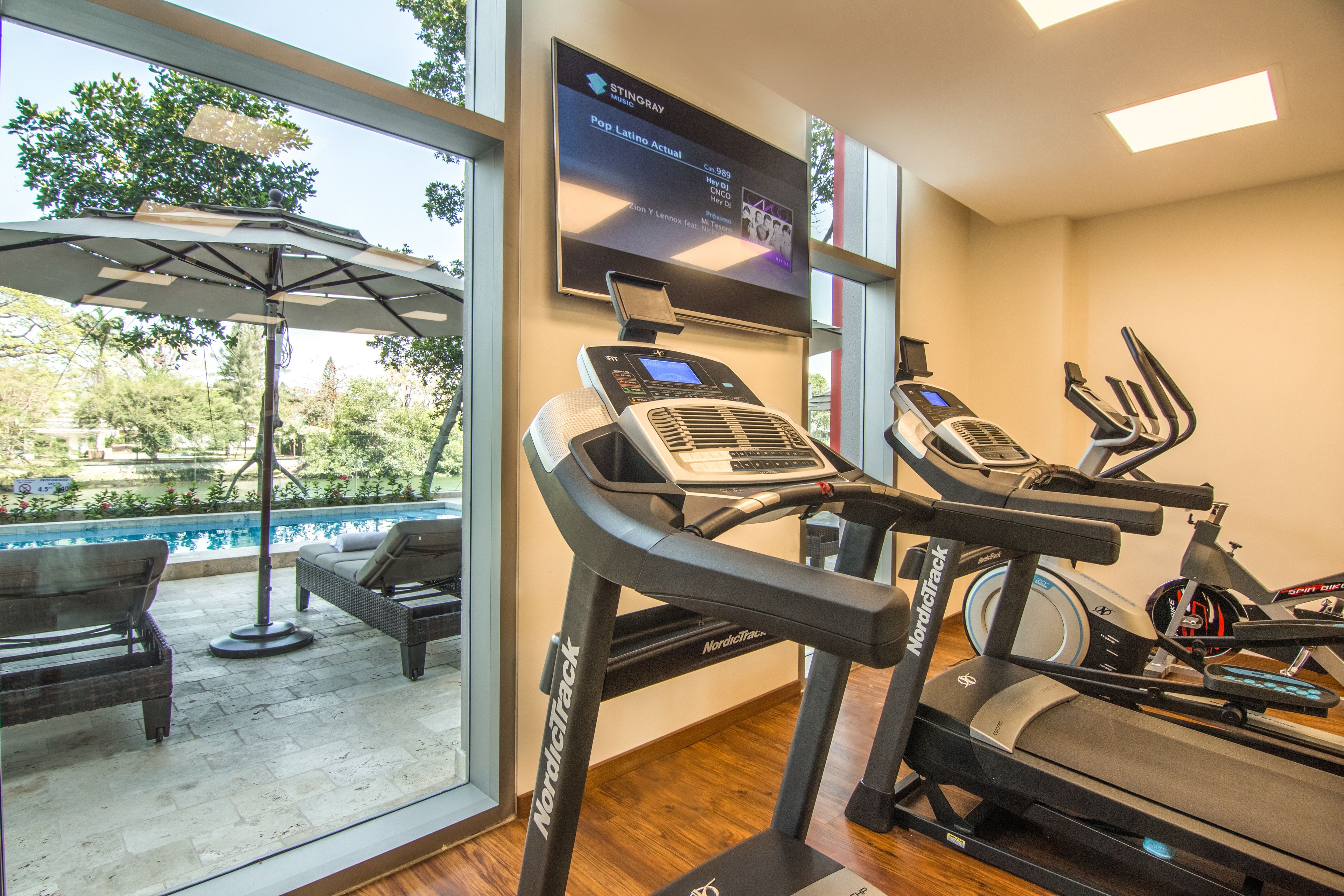 Un gimnasio con cintas de correr, una bicicleta estática y un área de piscina con sillones de descanso.