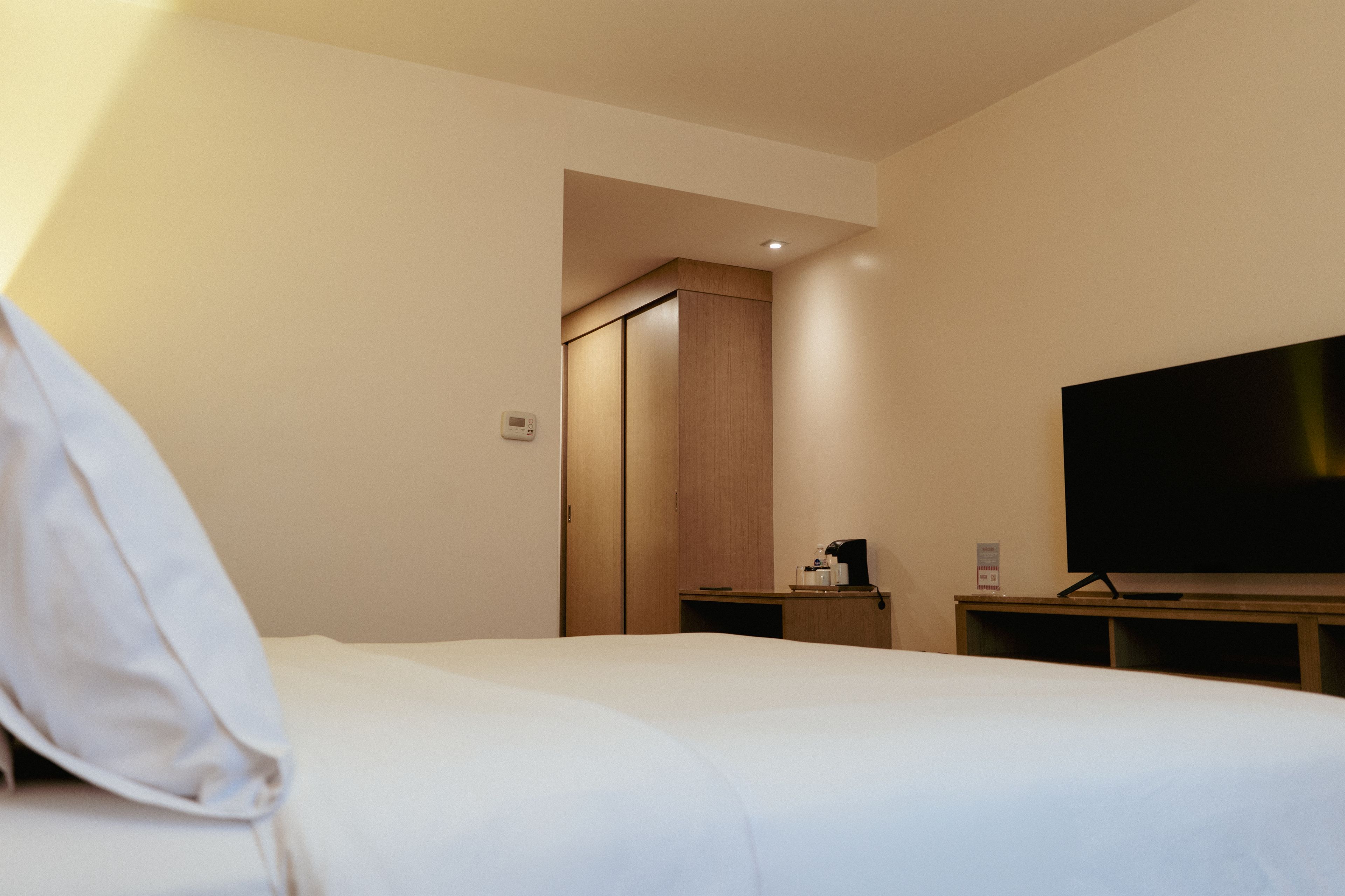 A hotel room with a bed, a television, a coffee maker, and a wardrobe.
