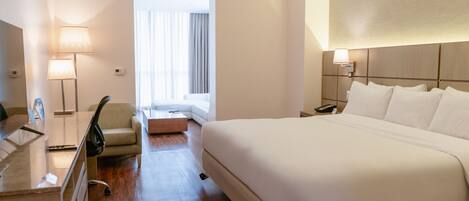A hotel room with a bed, a desk, a chair, a bedside table, and a lamp.