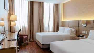 Habitación de hotel con dos camas, un escritorio, una silla y una mesita de noche con teléfono.