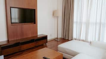 Una sala moderna con una televisión de pantalla plana montada en un mueble de madera, una lámpara de pie, un sofá blanco y una mesa de centro con controles remotos.